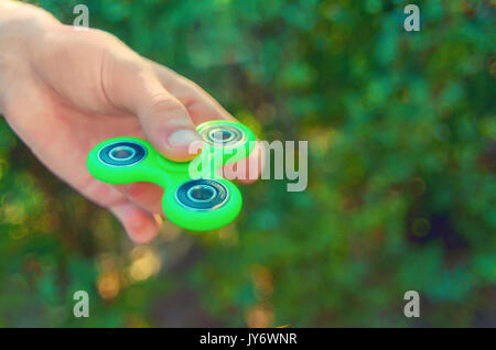 Teenager hand mit trendigen antistress Gadget zappeln Spinner. Mann spielt mit grünen Spinner im Freien auf der hellen Bokeh. Flache Freiheitsgrad. Stockfoto