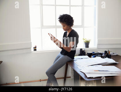 Junge Geschäftsfrau sitzt am Schreibtisch mit Phone im Büro Stockfoto