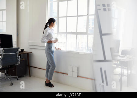 Junge Geschäftsfrau in Kaffee schaut aus Office Fenster Stockfoto