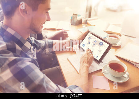 Fröhlicher junger Geschäftsmann studieren Statistiken auf seinem Tablet Stockfoto