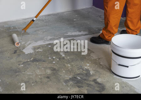 Innere der Wohnung renoviert. Mann hält eine Walze und setzt Grundierung auf Betonboden Stockfoto