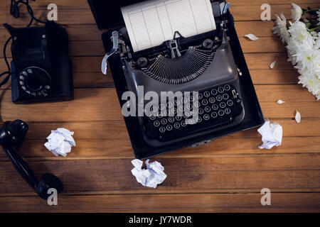 Ansicht von oben der Schreibmaschine durch Telefon und zerknittertes Papier auf Holz- Tabelle Stockfoto