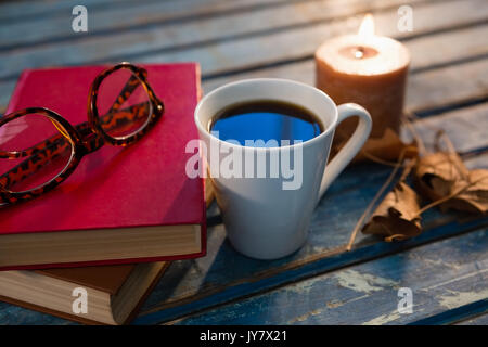 In der Nähe von Kaffee Tasse mit Brillen und Bücher von beleuchtet Kerze auf hölzernen Tisch Stockfoto