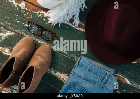 Hohe Betrachtungswinkel von Schuh- und Jeans mit persönlichen Accessoires auf hölzernen Tisch Stockfoto