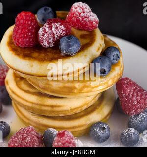 Stapel Pfannkuchen mit Himbeeren und Blaubeeren und Honig Abtropfen der Seite. Tight square Erntegut Stockfoto