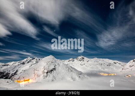 Der Damm und die Häuser im Dorf Montespluga, beleuchtet durch den Vollmond in einer Winternacht, Valchiavenna. Stockfoto