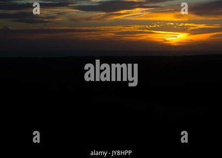 Ditchling Beacon, Sussex, UK. Ein tief orange Sonnenuntergang über der Silhouette Landschaft von Sussex. Stockfoto