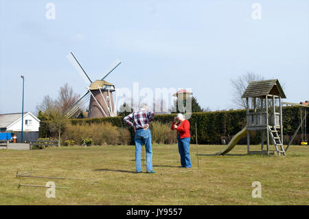 Ältere Paare versuchen, ein Zelt auf einem Campingplatz in der Neherlands mit einer Windmühle in den Hintergrund zu setzen Stockfoto