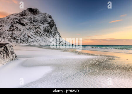 Wellen Fortschritte in Richtung Strand von schneebedeckten Gipfeln im Morgengrauen umgeben. Uttakleiv Lofoten norwegen Europa Stockfoto