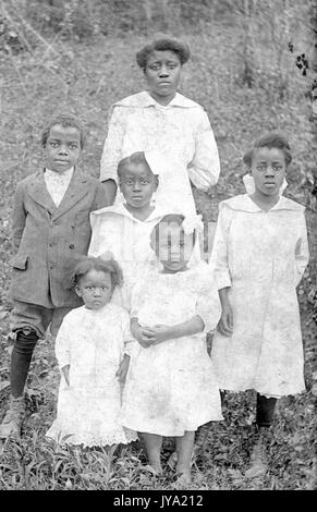 Portrait einer afrikanischen amerikanischen Mutter und ihre fünf Kinder stehen auf einem grasbewachsenen Hügel, alle Mädchen sind in hellen Kleidern und der Junge in einen dunklen Anzug, 1920. Stockfoto