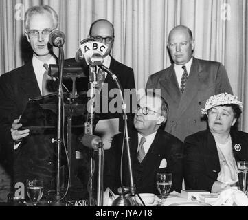 Das amerikanische Fernsehen host Lynn Poole steht an ein spezielles Mikrofon mit ABC aufgedruckt, Führungskräfte Ben Cohen und Dr Allen B DuMont stehen weiter hinter ihm, andere Gäste D Drewry und Dorothy Lewis sitzen vor Cohen und DuMont, 1955. Stockfoto