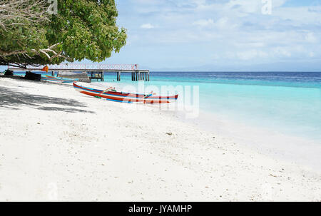 Rot weiss blau gefärbten kleinen leeren Kanu boot auf einer tropischen weißen Sandstrand mit blauen Ozean Wasser an einem sonnigen Tag, Indonesien gestrandet. Stockfoto