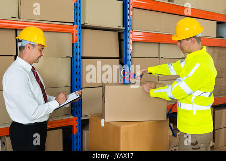 Manager unter Hinweis auf die Zwischenablage und Arbeiter Taping Box im Lager Stockfoto