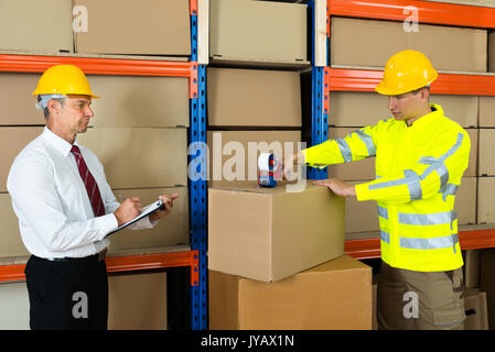 Manager unter Hinweis auf die Zwischenablage und Arbeiter Taping Box im Lager Stockfoto