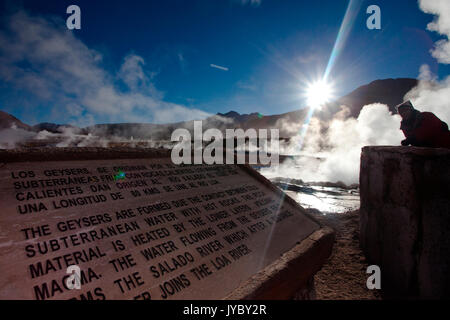 Eine Informationstafel bietet Informationen für Touristen, die die Geysire von El Tatio, deren Dämpfe von der Sonne beschienen werden. Im Hintergrund. Stockfoto