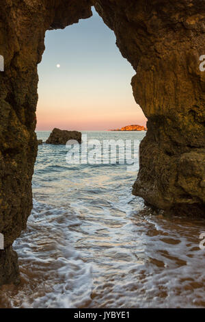 Eine Wasserhöhle, Frames den Ozean durch die Farben der Morgenröte im Praia da Rocha Portimão Bezirk Faro Algarve Portugal Europa beleuchtet Stockfoto