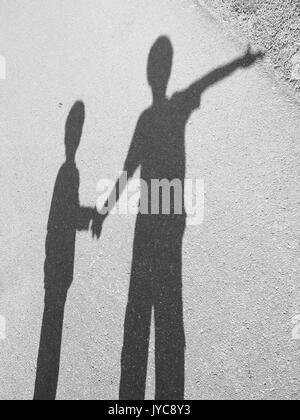 Schatten auf dem Bürgersteig durch zwei Kinder halten sich an den Händen, einer auf etwas in der Ferne zeigt. Stockfoto