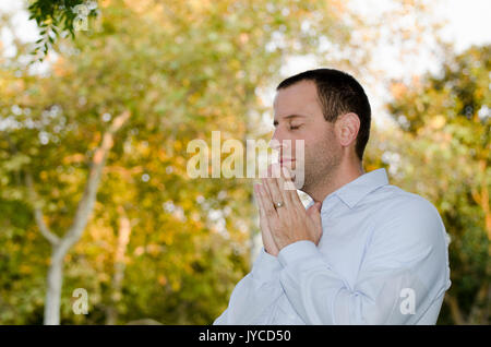 Business Mann alleine draußen mit Bäumen im Hintergrund zu beten. Stockfoto