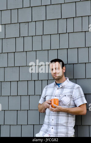 Man gegen eine Wand Holding eine Kaffeetasse lehnend. Stockfoto