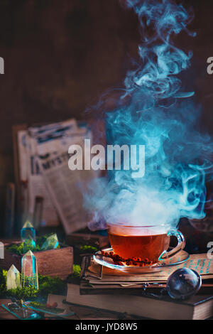 Dampfenden Glas Tasse Tee mit Kräutern und Beeren in eine magische Stillleben mit Moos und Kristallen. Stockfoto