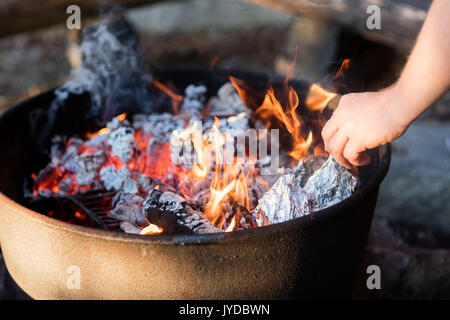 Nahaufnahme der Hand Grillen, DIE VON EINER FOLIE UMHÜLLT WIRD Auf der Feuerstelle Stockfoto