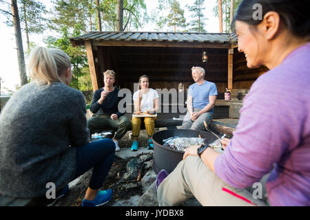 Freunde sprechen, während Sie Essen, die von der Feuerstelle im Wald Stockfoto
