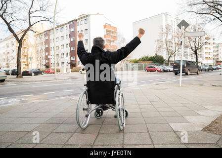 Rückansicht eines behinderten Menschen im Rollstuhl mit der Hand angehoben Stockfoto