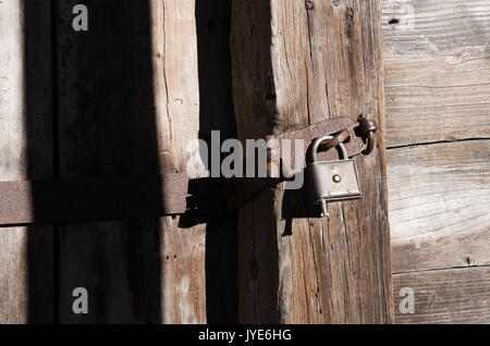 Neue Bügeleisen Schloss auf dem alten Metall Vorrichtung hängenden auf Holzbalken, Textur, horizontal Farbe Foto Stockfoto