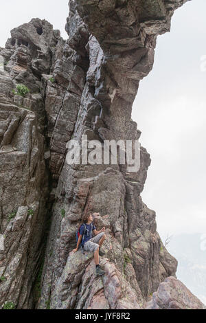 Wanderer sitzt auf den Felsen der Natural Arch Col de Bavella (Pass von Bavella) Solenzara Korsika Frankreich Europa Stockfoto