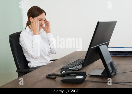 Geschäftsfrau in Kopf Schmerzen sitzen in der Nähe der Computer am Schreibtisch im Büro Stockfoto