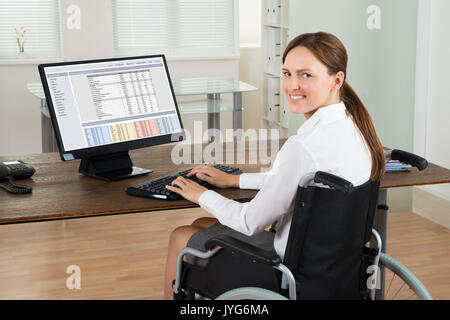 Junge glücklich Deaktiviert Geschäftsfrau auf Rollstuhl mit Computer im Büro Stockfoto