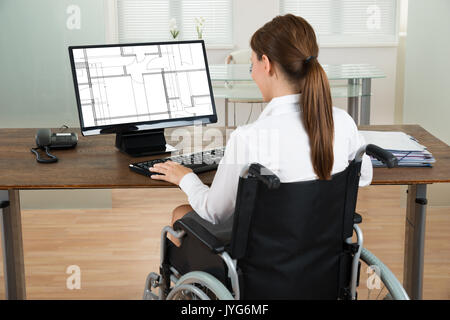 Junge weibliche Architekten auf Rollstuhl bei Blueprint auf dem Computer im Büro Stockfoto