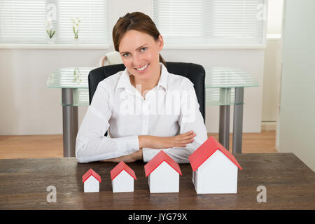 Happy Geschäftsfrau mit unterschiedlichen Größe des Hauses Modelle am Schreibtisch Stockfoto