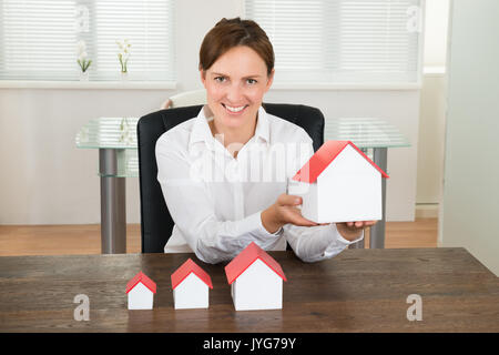 Happy Geschäftsfrau mit Haus Modelle auf hölzernen Schreibtisch im Büro Stockfoto