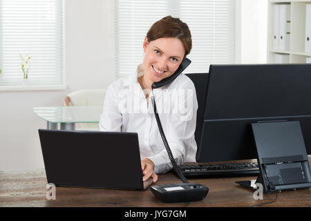 Glückliche junge geschäftsfrau am Telefon Sprechen während der Arbeit am Laptop im Büro Stockfoto