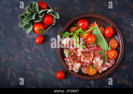 Gebratener Speck und Tomaten in der Platte auf einem dunklen Hintergrund. Flach. Ansicht von oben. Stockfoto