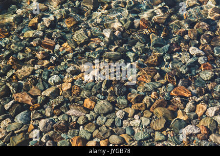 Durch die Dicke des transparentes Wasser sehen Sie das untere bestehend aus Kiesel, Steine, Sand. Hintergrund von einem runden Stein Kieselsteine am Stockfoto