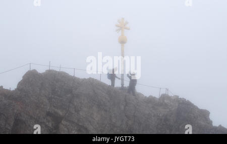 Grainau, Deutschland. 19 Aug, 2017. Zwei Bergsteiger stand neben dem Gipfelkreuz im Regen und Nebel auf der Zugspitze in Grainau, Deutschland, 19. August 2017. Foto: Sven Hoppe/dpa/Alamy leben Nachrichten Stockfoto