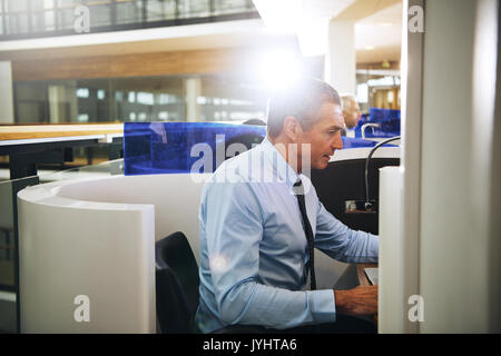 Seitliche Sicht auf die Arbeit im Büro erwachsenen Mann sitzen und surfen Laptop am Arbeitsplatz. Stockfoto