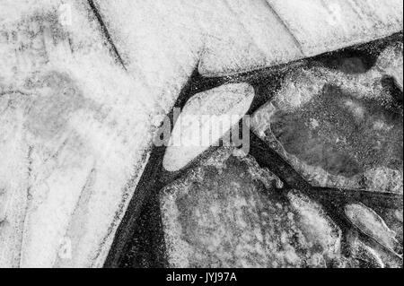 Gefrorene Pfützen mit Blätter unter Eisdecke, Muster und abstrakte Bilder gefroren, mit Blättern von Eis Teile Stockfoto