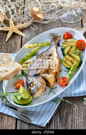 Gegrillte Goldbrasse mit gemischten Rosmarin Gemüse auf einer ovalen weißen Fischplatte serviert. Stockfoto