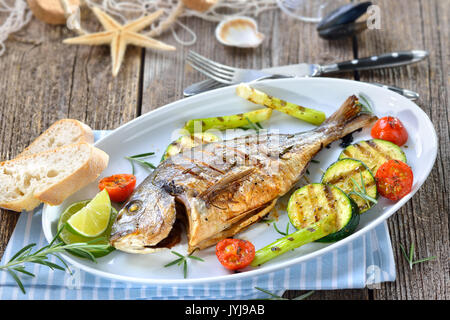 Gegrillte Goldbrasse mit gemischten Rosmarin Gemüse auf einer ovalen weißen Fischplatte serviert. Stockfoto