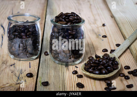 Kaffeebohnen in einem Glas und Löffel aus Holz, Holztisch, schwarzer Hintergrund Stockfoto