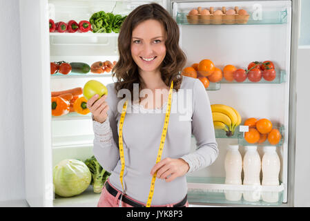 Glückliche Frau mit Maßband und grüner Apfel in der Nähe des offenen Kühlschrank mit gesunden Lebensmitteln Stockfoto