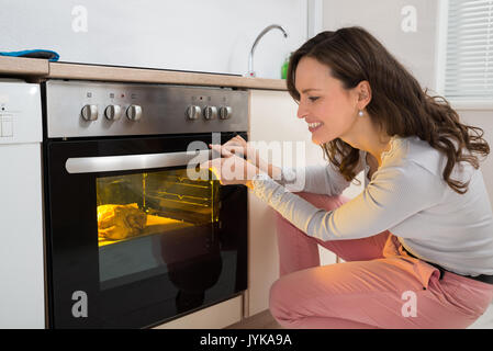 Glückliche Frau Rösten Hähnchenfleisch in Küche Backofen Stockfoto