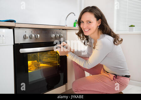 Glückliche Frau Rösten Hähnchenfleisch in Küche Backofen Stockfoto