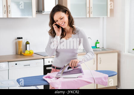 Junge Frau Gespräch am Handy während des Bügelns Tuch auf dem Bügelbrett Stockfoto