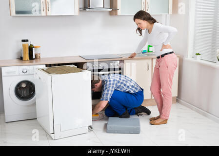 Junge Frau mit Blick auf die Arbeit der Handwerker Reparatur Geschirrspüler in der Küche Stockfoto