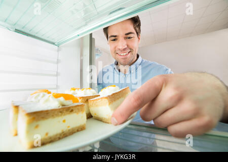 Porträt der jungen gutaussehenden Mann unter Kuchen Blick aus dem Kühlschrank Stockfoto