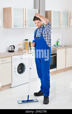 Junge männliche Arbeiter Reinigung Boden mit Mop im Haus Stockfoto